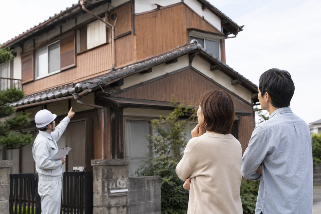 築40年以上の木造住宅でネズミの侵入口を点検する専門業者と住宅を見上げる夫婦